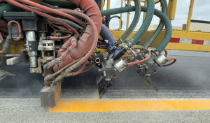Truck applying reflective beads to line work and monitoring bead flow during construction.