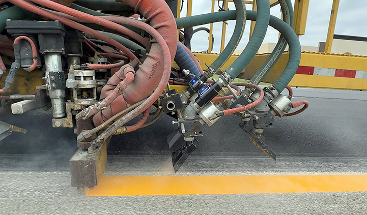 Truck applying reflective beads to line work and monitoring bead flow during construction.